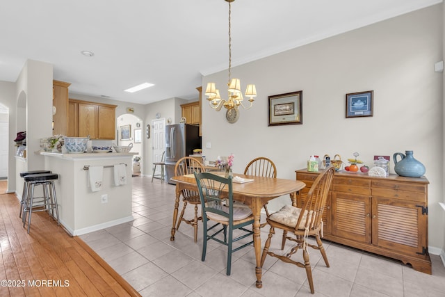 dining area with arched walkways, light tile patterned flooring, baseboards, and an inviting chandelier