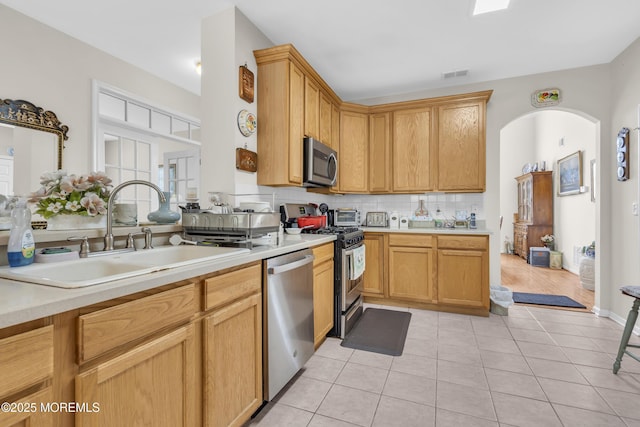 kitchen featuring light tile patterned floors, stainless steel appliances, light countertops, backsplash, and a sink