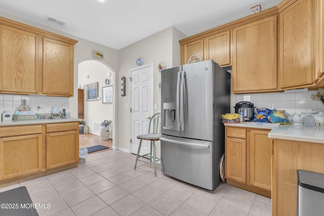 kitchen featuring arched walkways, tasteful backsplash, light countertops, visible vents, and stainless steel fridge with ice dispenser