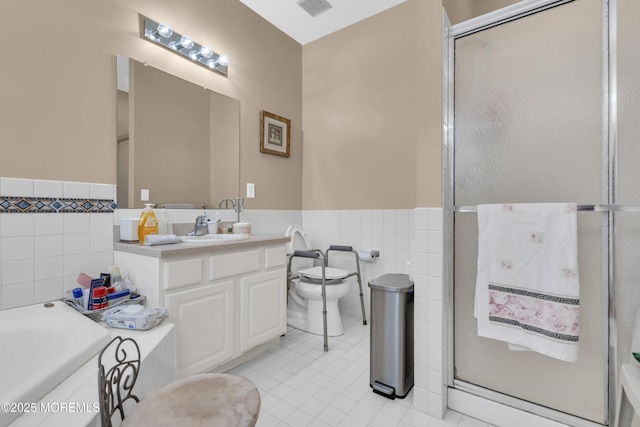 bathroom with toilet, a wainscoted wall, a garden tub, vanity, and tile walls