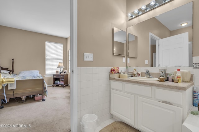 ensuite bathroom with connected bathroom, vanity, and tile walls