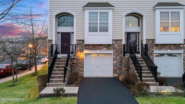 view of front of house with stone siding, aphalt driveway, an attached garage, and a shingled roof