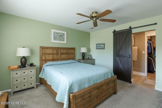 carpeted bedroom featuring ceiling fan, a barn door, a closet, and a spacious closet