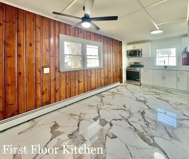 interior space featuring sink, wood walls, white cabinetry, appliances with stainless steel finishes, and a healthy amount of sunlight