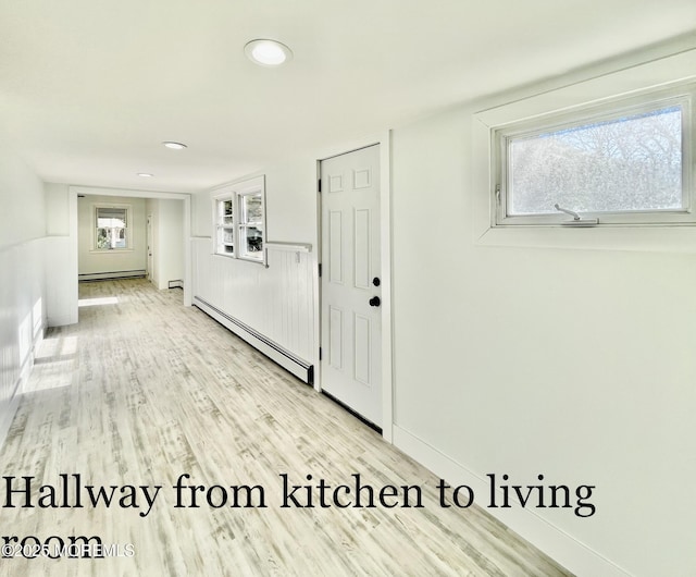 hallway with light wood-type flooring and a baseboard heating unit