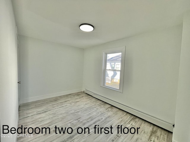 unfurnished room with a baseboard radiator and light wood-type flooring