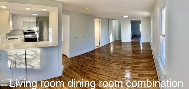 kitchen featuring white cabinetry, a baseboard radiator, sink, stainless steel appliances, and dark wood-type flooring