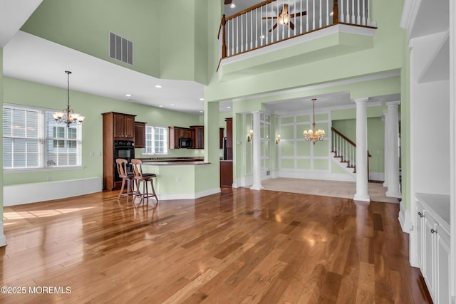 unfurnished living room with an inviting chandelier, light hardwood / wood-style floors, and ornate columns