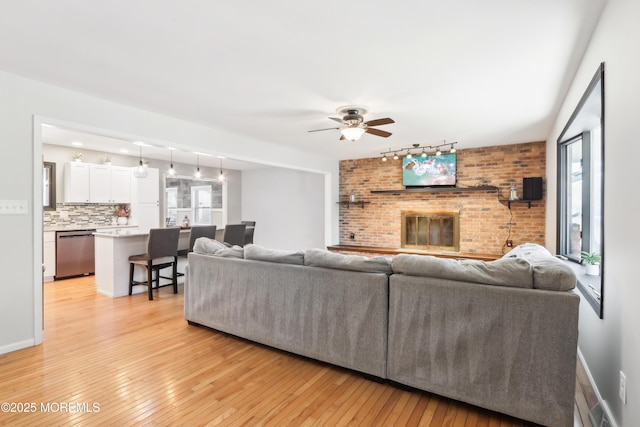 living room featuring a fireplace, track lighting, ceiling fan, and light wood-type flooring