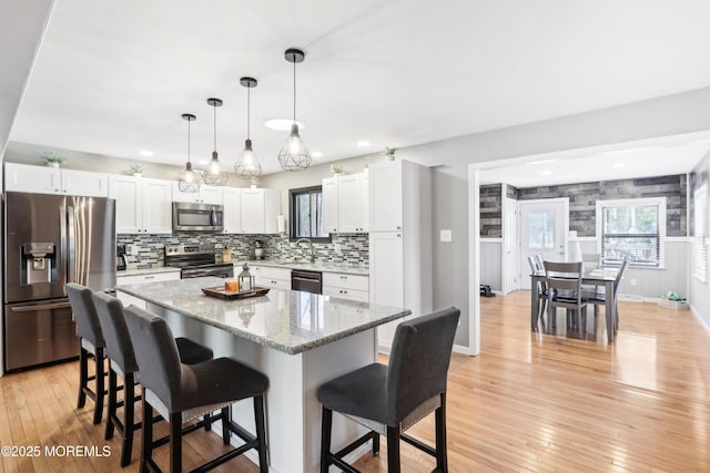 kitchen featuring white cabinetry, hanging light fixtures, a kitchen breakfast bar, a kitchen island, and stainless steel appliances