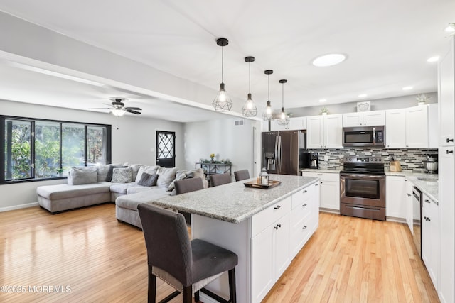 kitchen featuring a breakfast bar area, white cabinetry, appliances with stainless steel finishes, pendant lighting, and light stone countertops