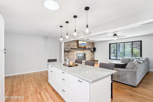 kitchen with decorative light fixtures, white cabinetry, a breakfast bar area, light stone counters, and light wood-type flooring