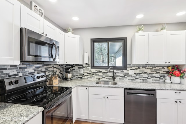 kitchen with light stone counters, stainless steel appliances, sink, and white cabinets