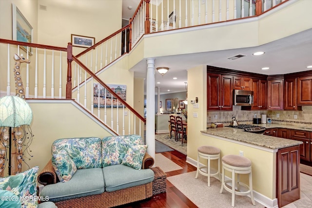 kitchen with decorative columns, a high ceiling, light hardwood / wood-style floors, light stone countertops, and decorative backsplash