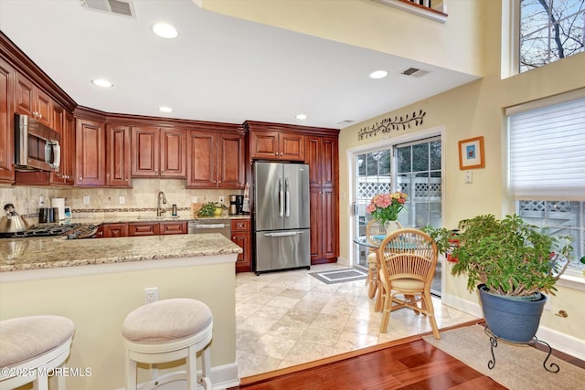 kitchen featuring light hardwood / wood-style flooring, stainless steel appliances, tasteful backsplash, light stone countertops, and kitchen peninsula