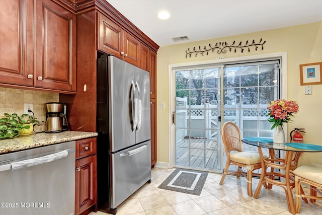 kitchen featuring light stone counters, stainless steel appliances, light tile patterned floors, and backsplash