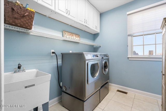 clothes washing area featuring separate washer and dryer, sink, light tile patterned floors, and cabinets