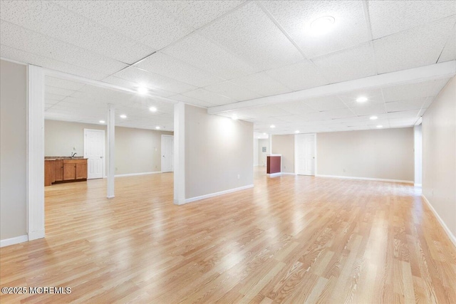 basement with light hardwood / wood-style flooring and a paneled ceiling