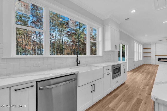 kitchen with stainless steel appliances, white cabinetry, ornamental molding, and light stone counters