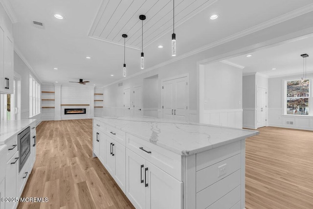 kitchen featuring white cabinetry, pendant lighting, light stone counters, and a spacious island