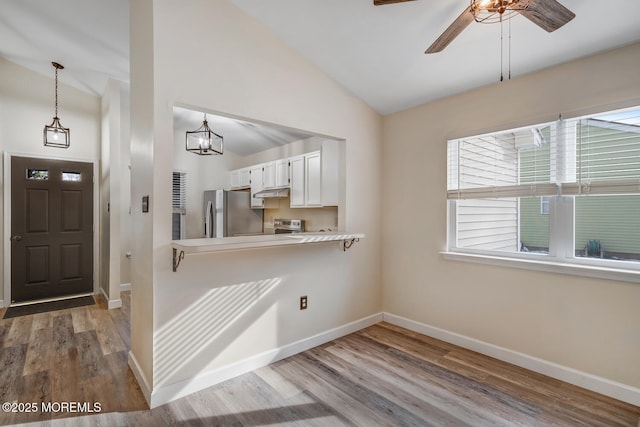 kitchen featuring hardwood / wood-style flooring, stainless steel refrigerator, white cabinets, decorative light fixtures, and vaulted ceiling