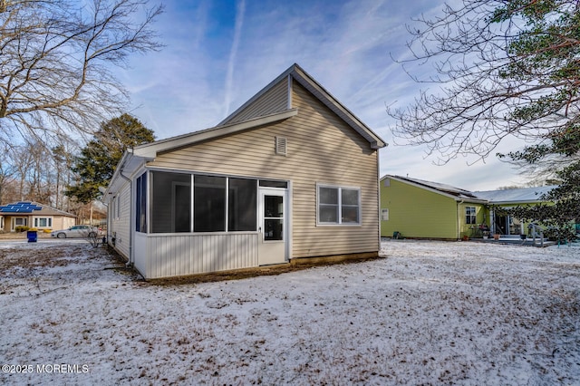 snow covered back of property with a sunroom