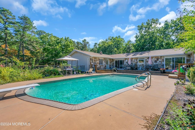 view of pool featuring grilling area, a diving board, and a patio area