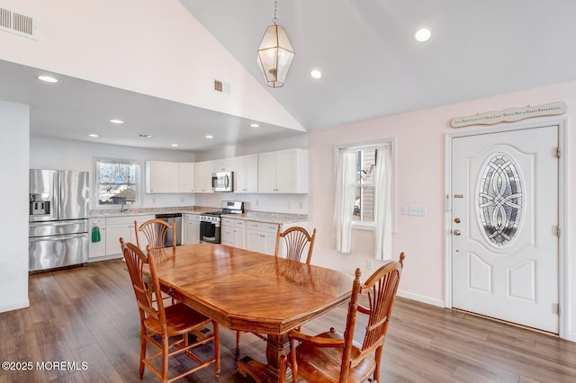 dining area with sink, light hardwood / wood-style floors, and high vaulted ceiling