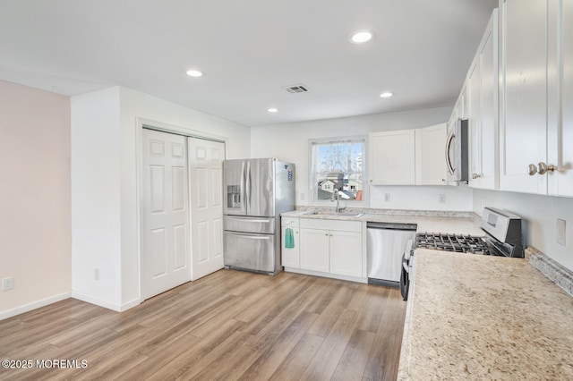 kitchen with sink, light stone counters, light hardwood / wood-style flooring, appliances with stainless steel finishes, and white cabinets