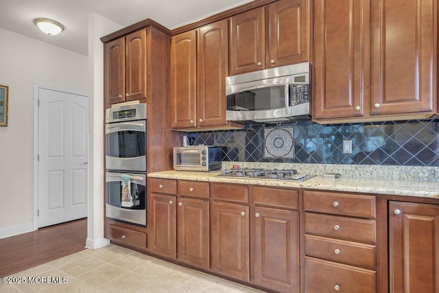 kitchen featuring light tile patterned floors, decorative backsplash, light stone countertops, and appliances with stainless steel finishes