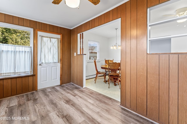 doorway to outside featuring light hardwood / wood-style flooring, ornamental molding, wooden walls, ceiling fan with notable chandelier, and a baseboard heating unit