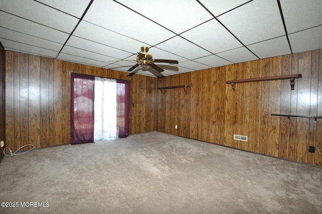 spare room with ceiling fan, carpet floors, a drop ceiling, and wooden walls