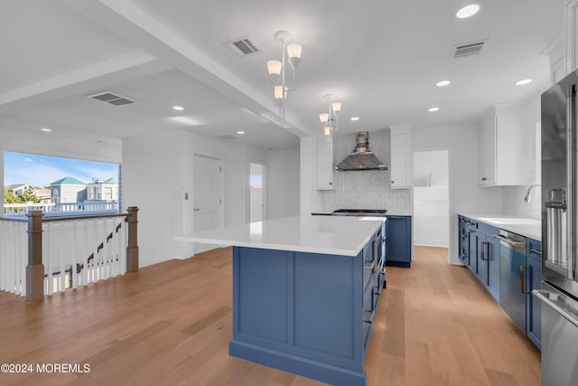 kitchen with blue cabinetry, white cabinetry, wall chimney exhaust hood, and appliances with stainless steel finishes