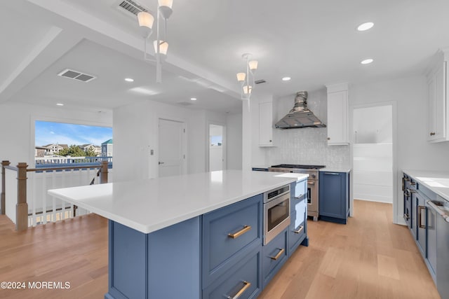 kitchen featuring blue cabinetry, custom exhaust hood, hanging light fixtures, stainless steel appliances, and white cabinets