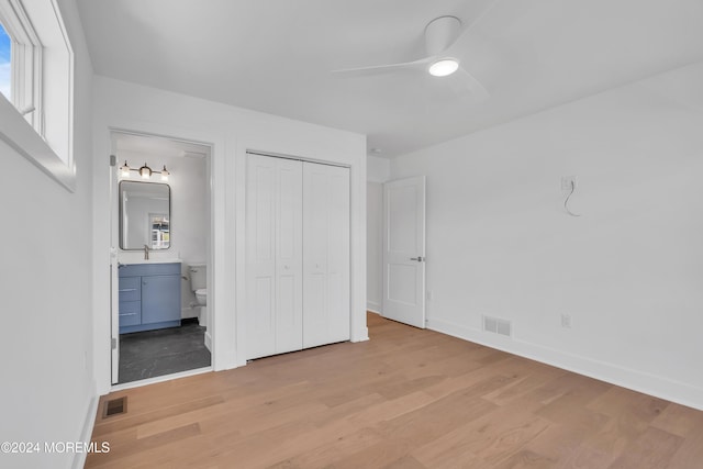 unfurnished bedroom featuring a closet, ensuite bathroom, ceiling fan, and light wood-type flooring