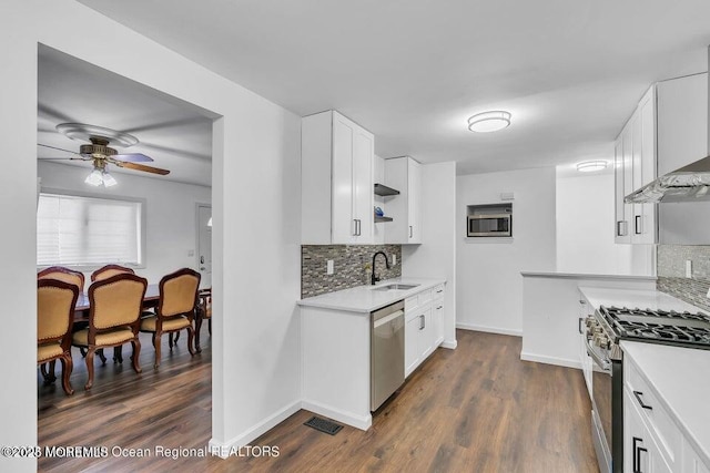 kitchen with dark wood-type flooring, sink, white cabinetry, stainless steel appliances, and wall chimney range hood