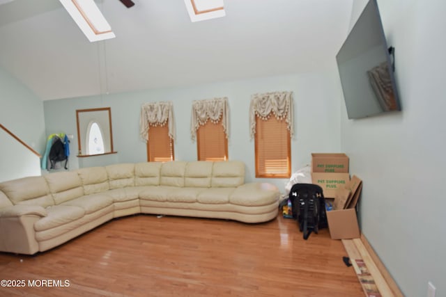 living room with a ceiling fan, vaulted ceiling with skylight, and wood finished floors