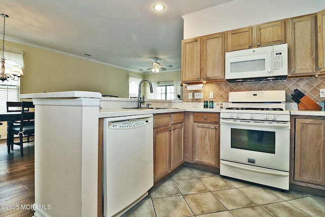 kitchen with decorative light fixtures, sink, kitchen peninsula, crown molding, and white appliances