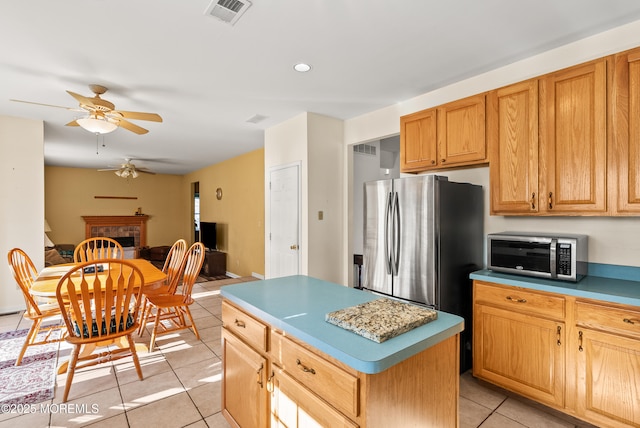 kitchen featuring light tile patterned flooring, a kitchen island, a fireplace, ceiling fan, and stainless steel appliances