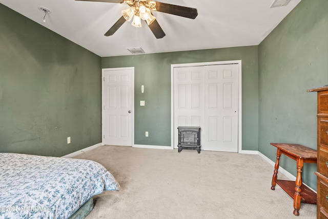 carpeted bedroom with ceiling fan, a closet, and a wood stove