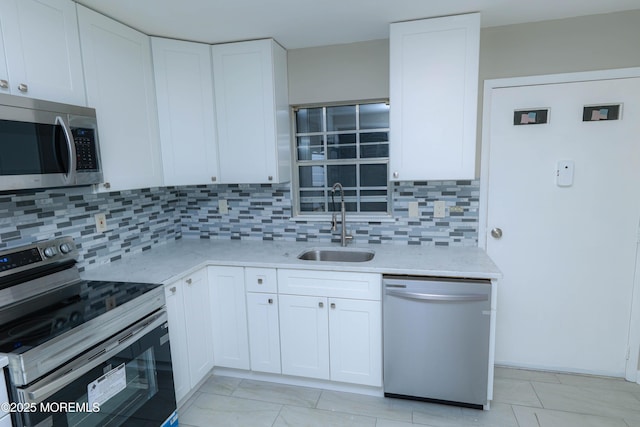 kitchen with sink, appliances with stainless steel finishes, white cabinetry, backsplash, and light stone countertops