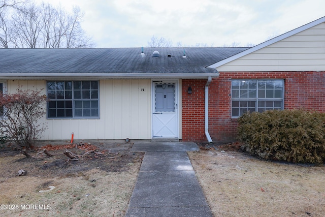 view of exterior entry with a shingled roof and brick siding