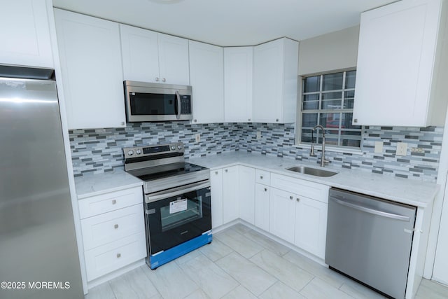 kitchen with light stone counters, stainless steel appliances, a sink, white cabinets, and backsplash