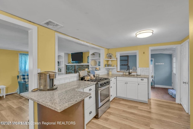 kitchen featuring white cabinetry, sink, light stone counters, kitchen peninsula, and stainless steel range with gas stovetop