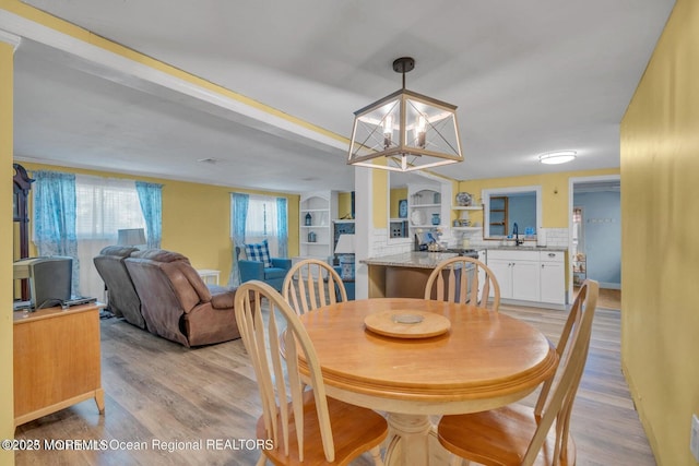 dining area with an inviting chandelier, sink, and light hardwood / wood-style flooring