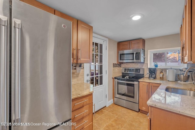 kitchen with light tile patterned flooring, sink, light stone counters, tasteful backsplash, and stainless steel appliances