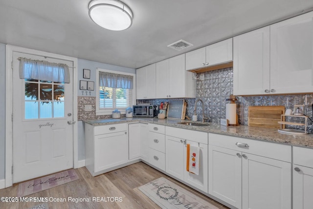 kitchen with white cabinetry, light stone countertops, sink, and light wood-type flooring