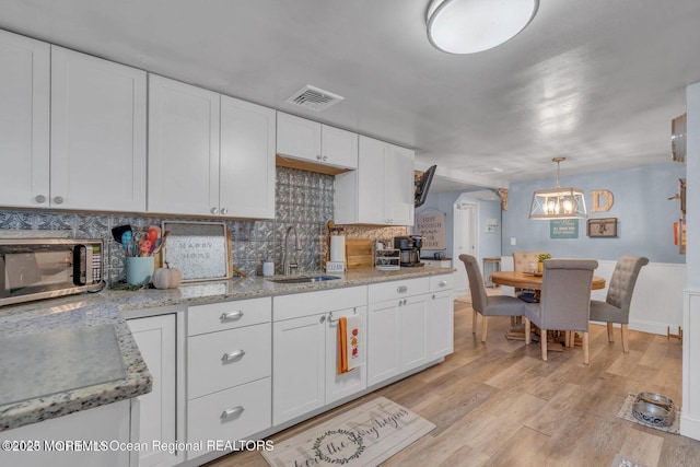 kitchen featuring sink, hanging light fixtures, light hardwood / wood-style floors, decorative backsplash, and white cabinets