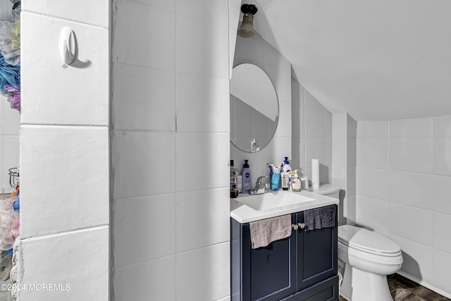 bathroom with lofted ceiling, vanity, toilet, and tile walls