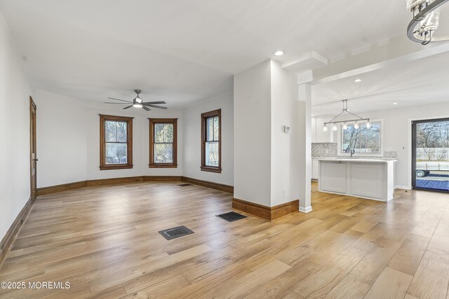 unfurnished living room with sink, ceiling fan with notable chandelier, and light wood-type flooring